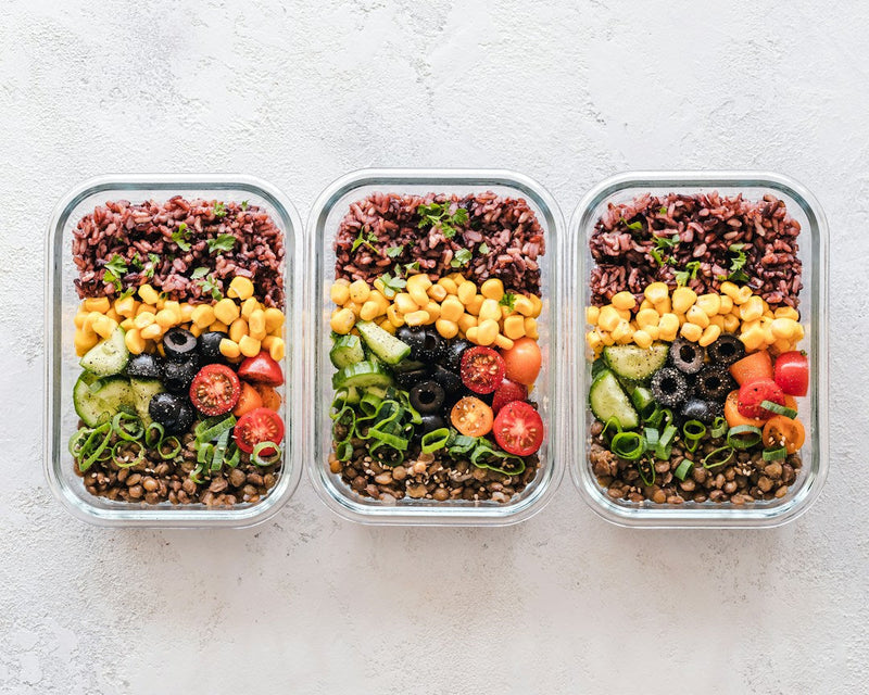 Three plant-based meal containers with lentils, grains, corn and colorful vegetables