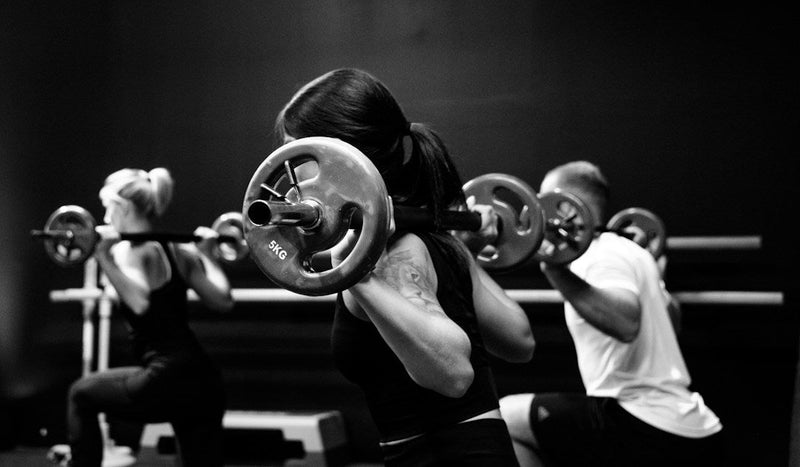 Three people training together with barbells in a fitness class