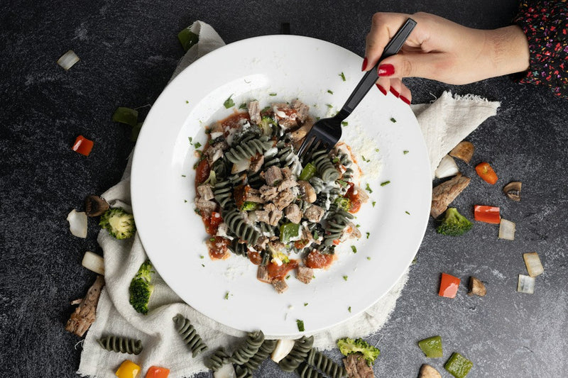 A prepared pasta dinner with vegetables and protein on a white plate
